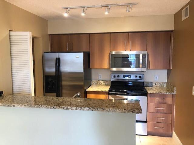 1000 Crystal Way, Unit C Delray Beach, FL 33444 - Photo 2 of 10 a kitchen with stainless steel appliances wooden cabinets a stove and a refrigerator
