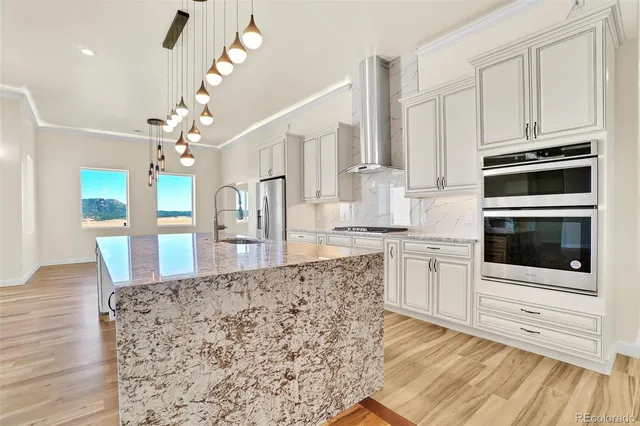 a kitchen with stainless steel appliances kitchen island granite countertop a stove top oven a sink dishwasher and white cabinets with wooden floor