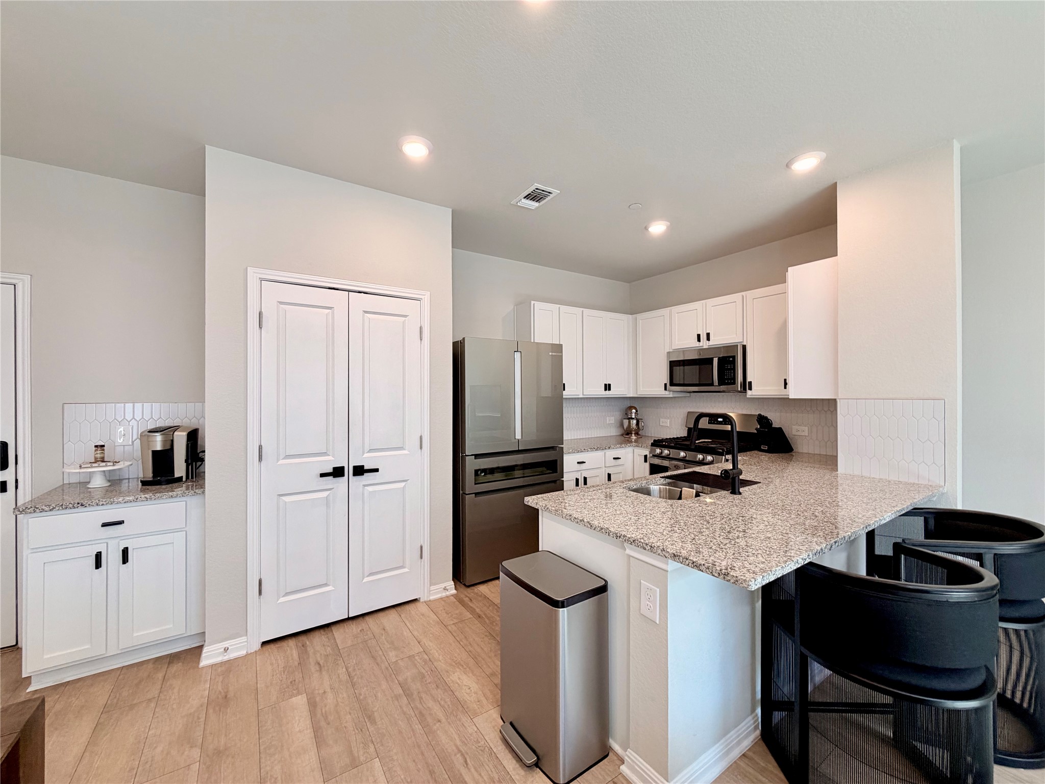 9015 Cattle Baron Path, Unit 1803 Austin, TX 78747 - Photo 4 of 23 Kitchen w/ backsplash, white cabinets, stainless steel appliances, a breakfast bar, black cabinet pulls, and light stone countertops