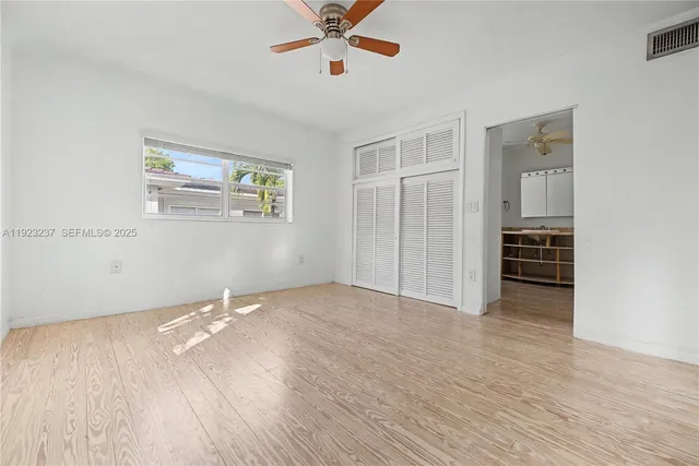 a view of an empty room with wooden floor and a ceiling fan