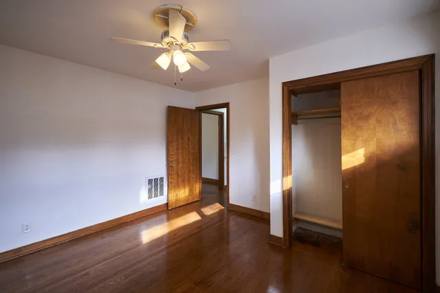 a view of an empty room with wooden floor and a ceiling fan