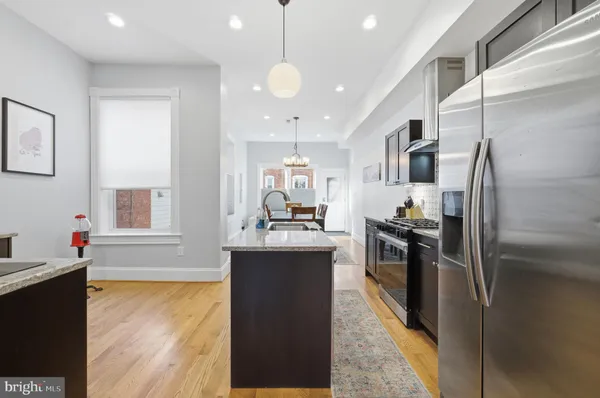 a kitchen with stainless steel appliances granite countertop a refrigerator a sink dishwasher a stove and white countertops with wooden floor
