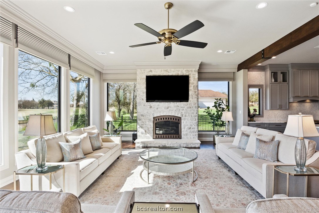 5202 Bourrone Court Bryan, TX 77802 - Photo 10 of 43 The living room boasts 11-ft ceilings, a stone-to-ceiling gas fireplace, and wall-to-wall windows framing the stunning golf course.