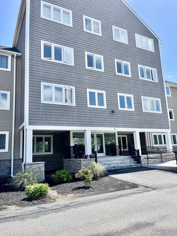 38 Dunham Road, Unit 303 Beverly, MA 01915 - Photo 3 of 12 a front view of a building with a yard and a garage