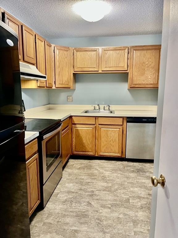 38 Dunham Road, Unit 303 Beverly, MA 01915 - Photo 8 of 12 a kitchen with granite countertop a sink stainless steel appliances wooden cabinets and a counter top space