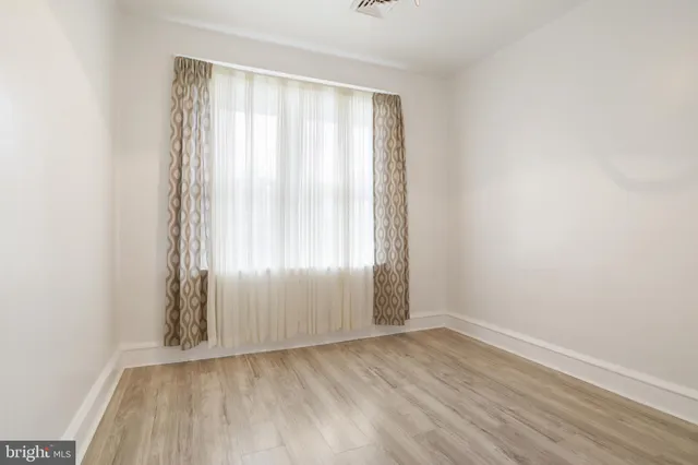 an empty room with wooden floor and windows with curtains