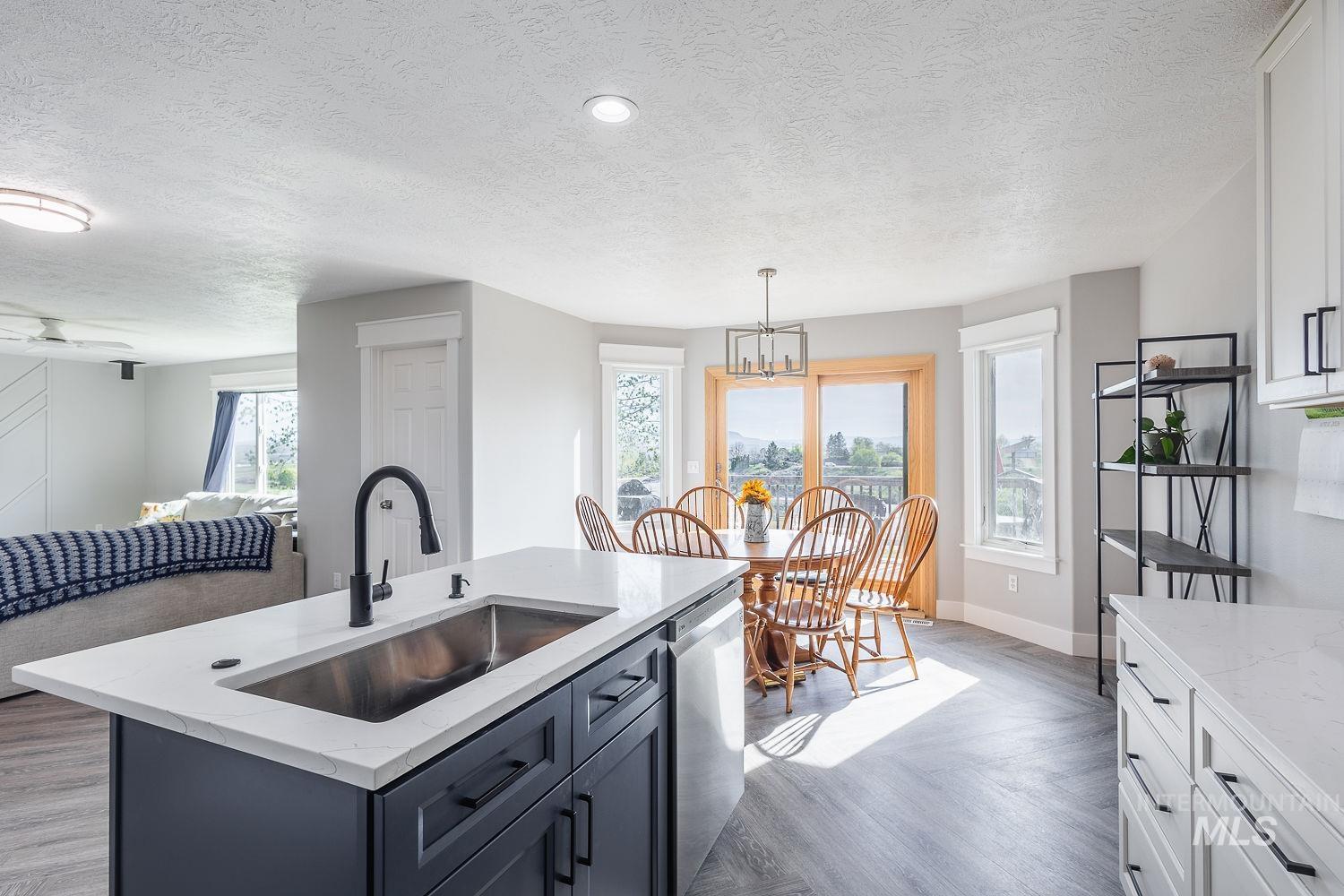 3950 Cassia Road New Plymouth, ID 83655 - Photo 11 of 26 Kitchen with parquet flooring, light stone countertops, dishwasher, a kitchen island with sink, and a textured ceiling