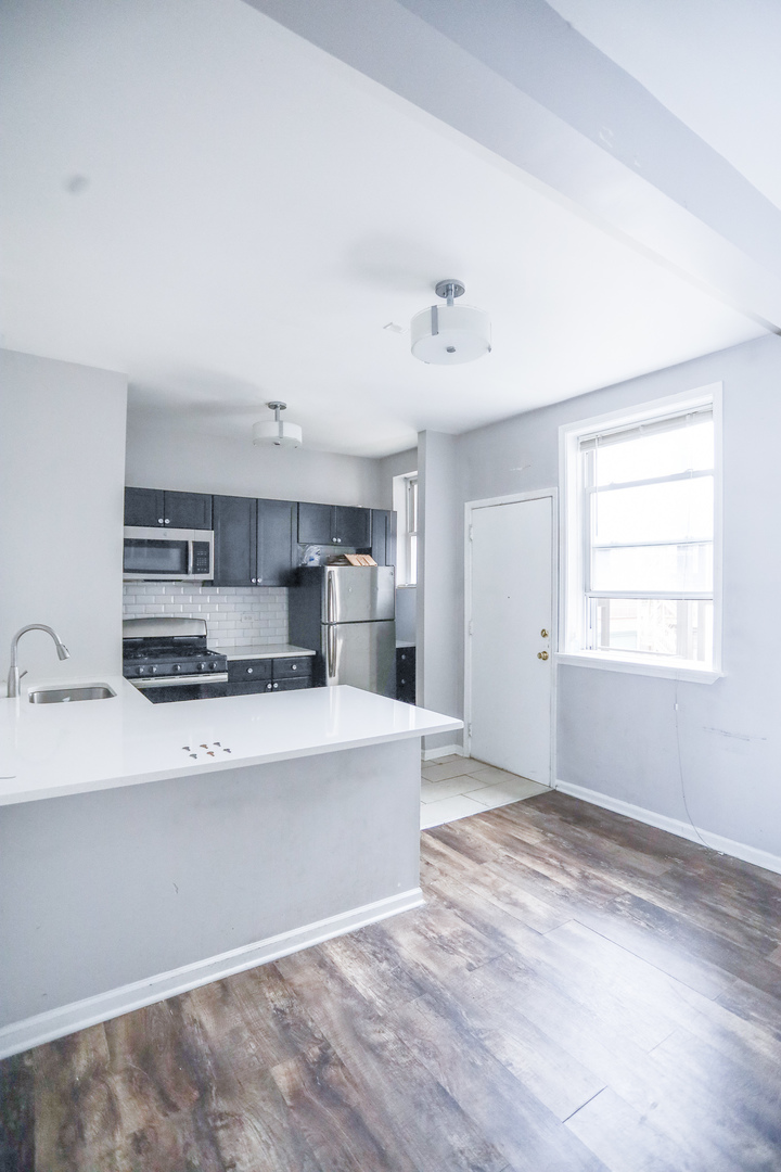 4400 North Magnolia Avenue, Unit 321 Chicago, IL 60640 - Photo 3 of 12 a large white kitchen with kitchen island a stove a sink dishwasher and a refrigerator with wooden floor