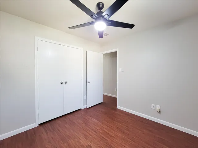 an empty room with wooden floor chandelier fan and windows