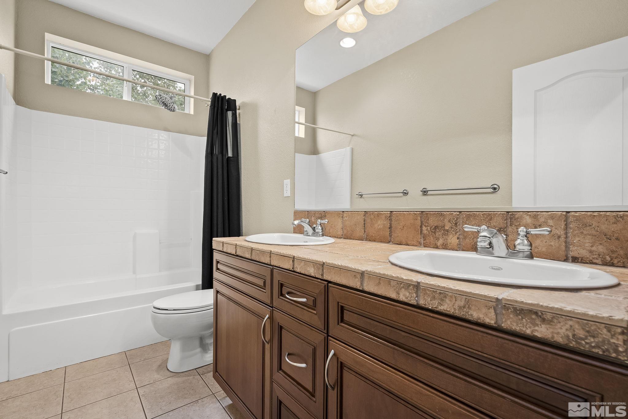 7144 Crest Hill Drive Reno, NV 89506 - Photo 22 of 28 a bathroom with a granite countertop toilet a sink and a mirror
