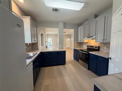 a kitchen with granite countertop a refrigerator a stove top oven and a sink with wooden floor
