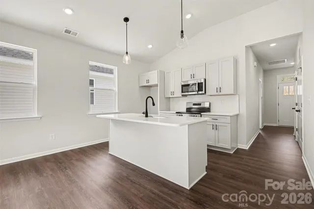 a kitchen with stainless steel appliances granite countertop a sink a stove a refrigerator and white cabinets with wooden floor