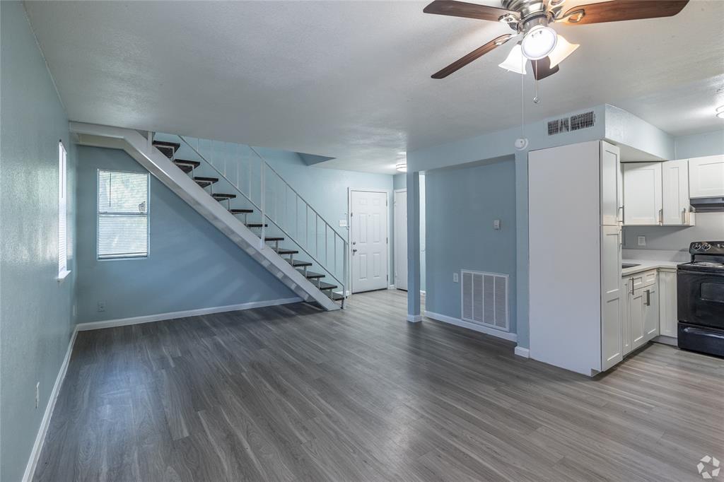 313 Rolston Road, Unit 315102 Irving, TX 75060 - Photo 2 of 8 Open-concept living space featuring wood-finish flooring, a ceiling fan with integrated lighting, and a partial kitchen with white cabinetry and a black range