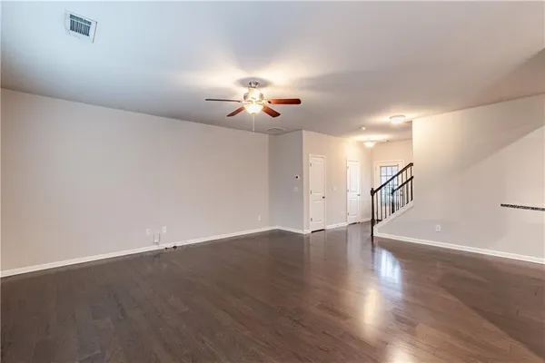 a view of an empty room with wooden floor and a ceiling fan