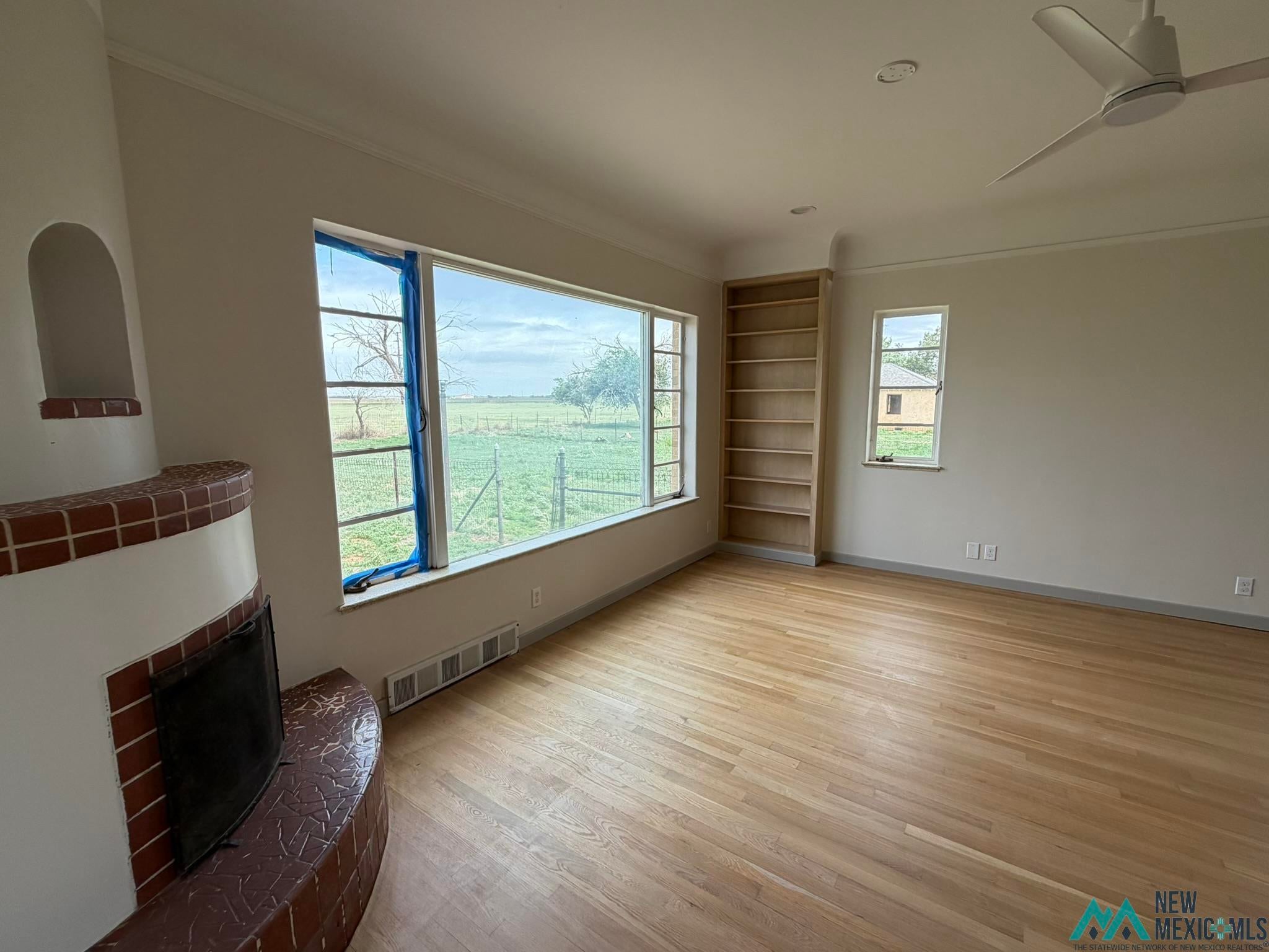 570 Curry Road North Clovis, NM 88101 - Photo 39 of 59 Spacious room featuring wood-finish flooring, a brick fireplace, a built-in shelving unit, and multiple windows