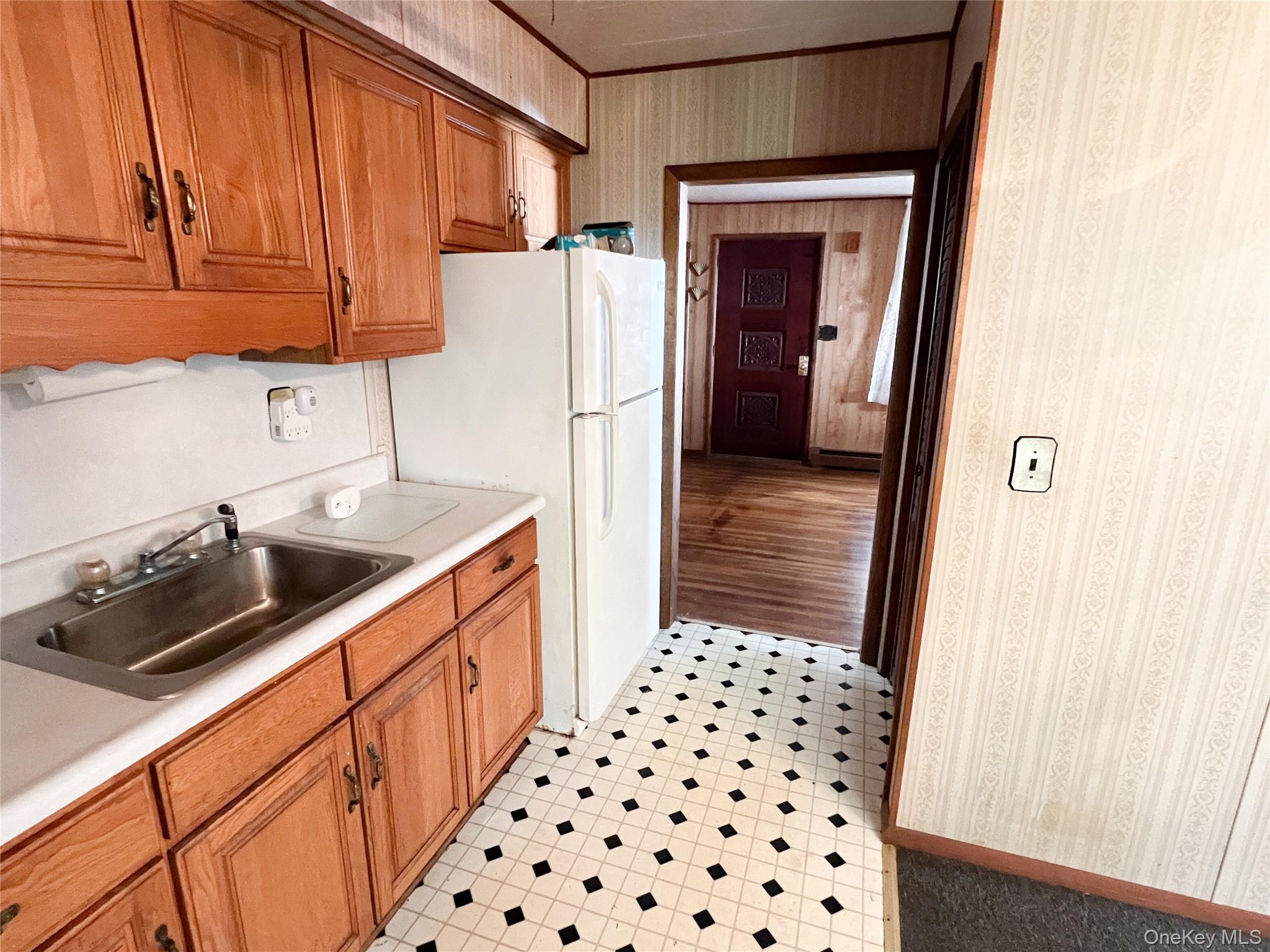 259 Tennanah Lake Road Roscoe, NY 12776 - Photo 5 of 11 Kitchen with brown cabinetry, wallpapered walls, light countertops, freestanding refrigerator, and baseboard heating