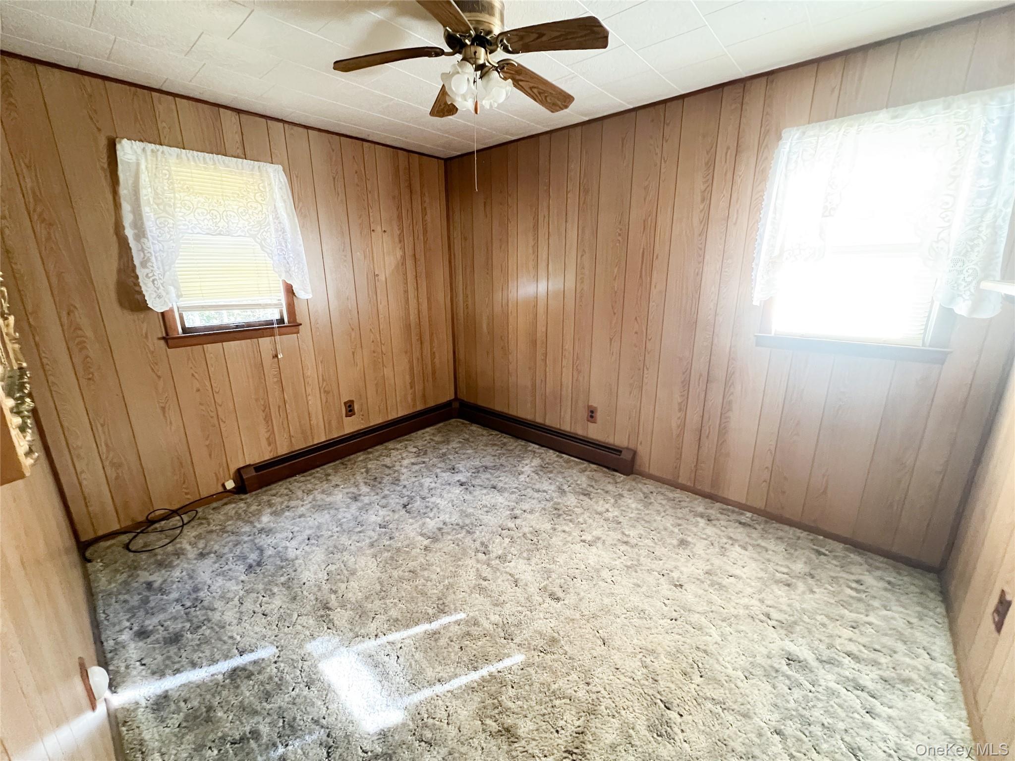 259 Tennanah Lake Road Roscoe, NY 12776 - Photo 8 of 11 Empty room with wooden walls, ceiling fan, and a baseboard heating unit