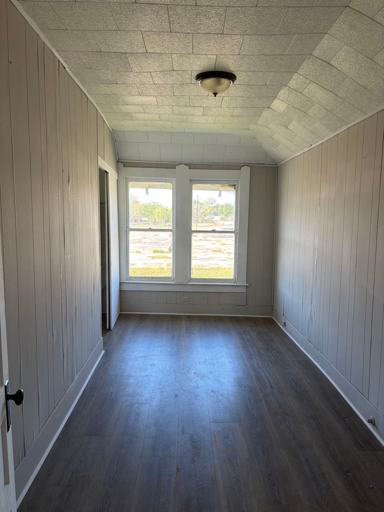 931 9th Avenue, Unit 2 Port Arthur, TX 77642 - Photo 4 of 9 This room features wood panel walls and a unique tiled ceiling, with a central light fixture. It has large windows for natural light and a wood-style floor, giving it a cozy and inviting feel.