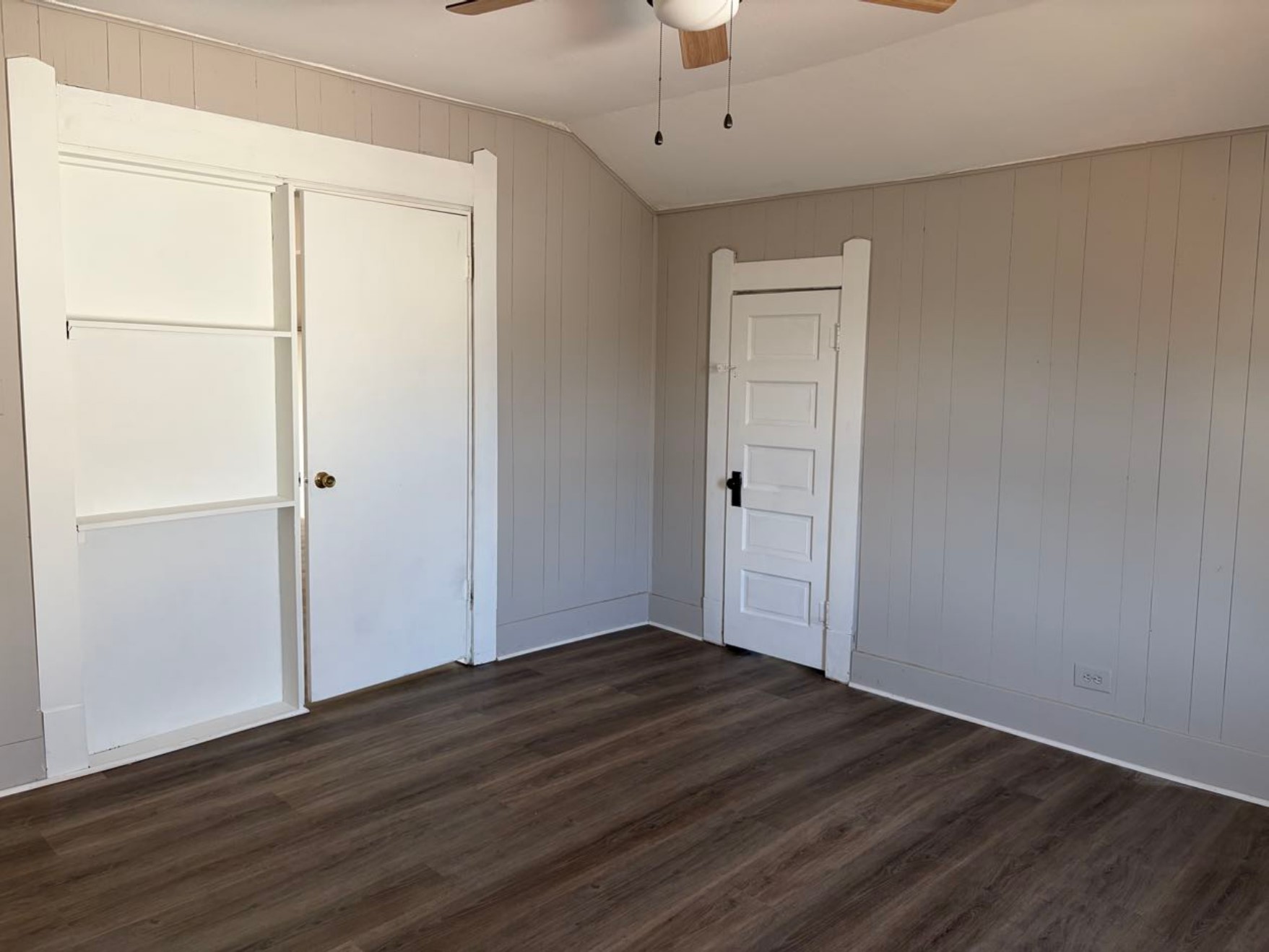 931 9th Avenue, Unit 2 Port Arthur, TX 77642 - Photo 5 of 9 Bedroom - This room features light gray paneled walls, warm wood flooring, and a ceiling fan. It includes two doors with white trim, offering a clean, inviting space with a cozy feel.