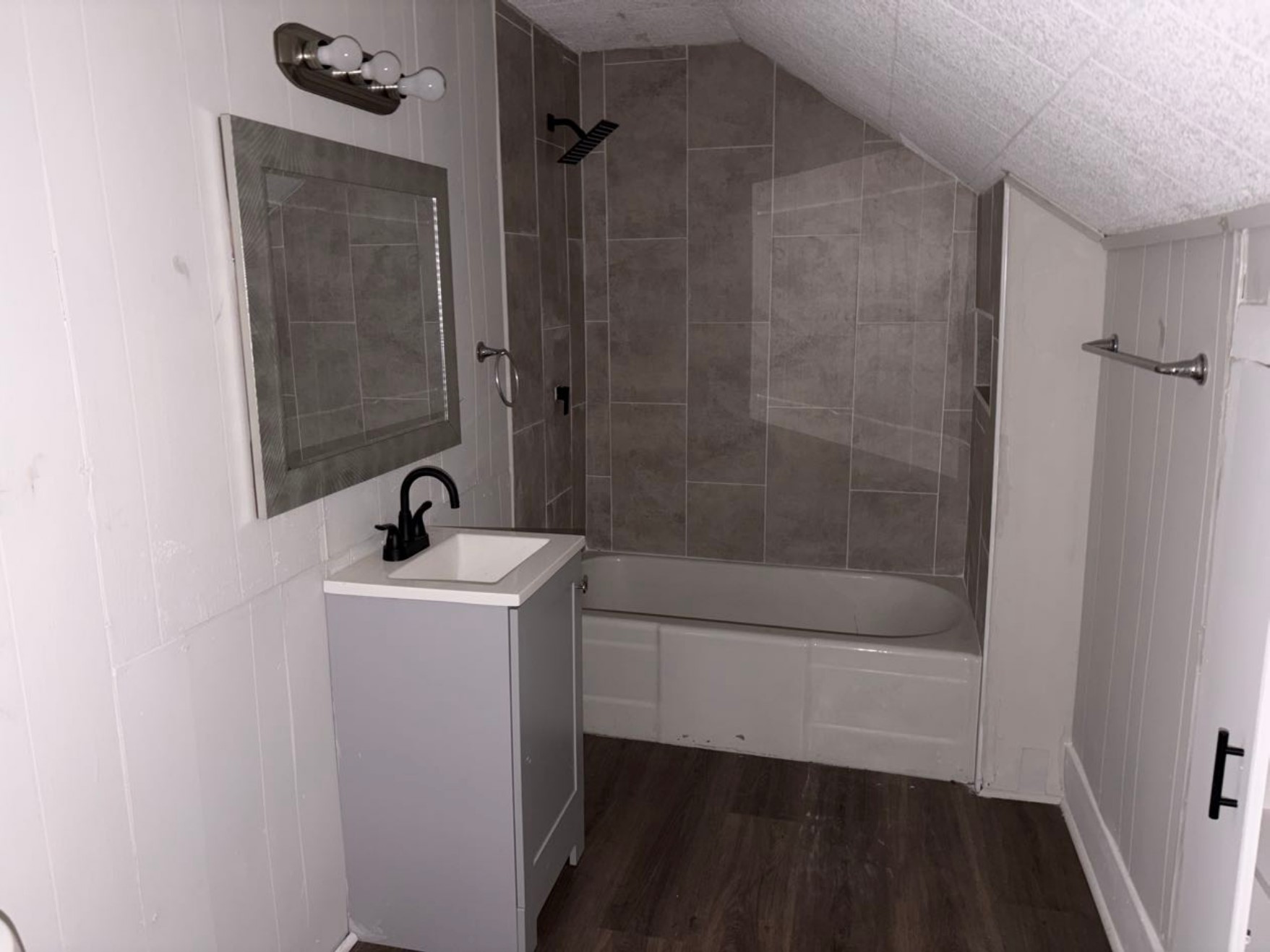 931 9th Avenue, Unit 2 Port Arthur, TX 77642 - Photo 9 of 9 Bathroom - Compact bathroom with a sloped ceiling, featuring a tiled shower and bathtub combo, modern vanity with a black faucet, a large mirror, and wood-style flooring.