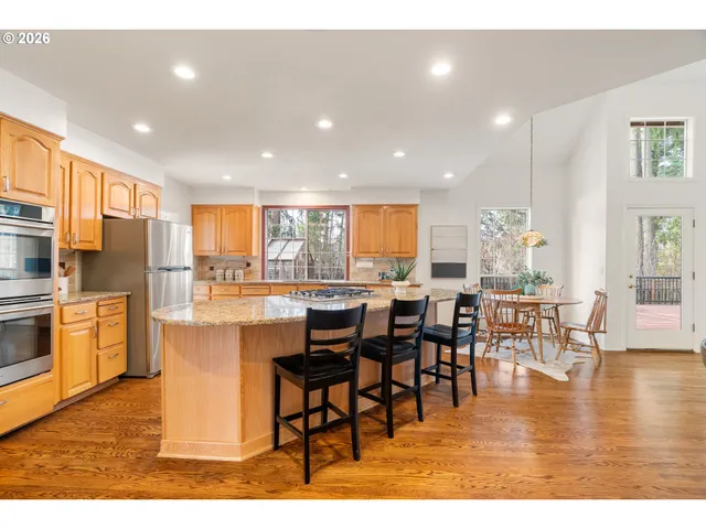 a dining hall with stainless steel appliances granite countertop a refrigerator a stove a dining table and chairs