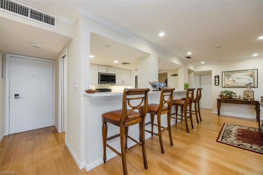 1900 Clifford Street, Unit 301 Fort Myers, FL 33901 - Photo 5 of 35 Kitchen featuring stainless steel microwave, light wood-style flooring, crown molding, white cabinets, and a breakfast bar area