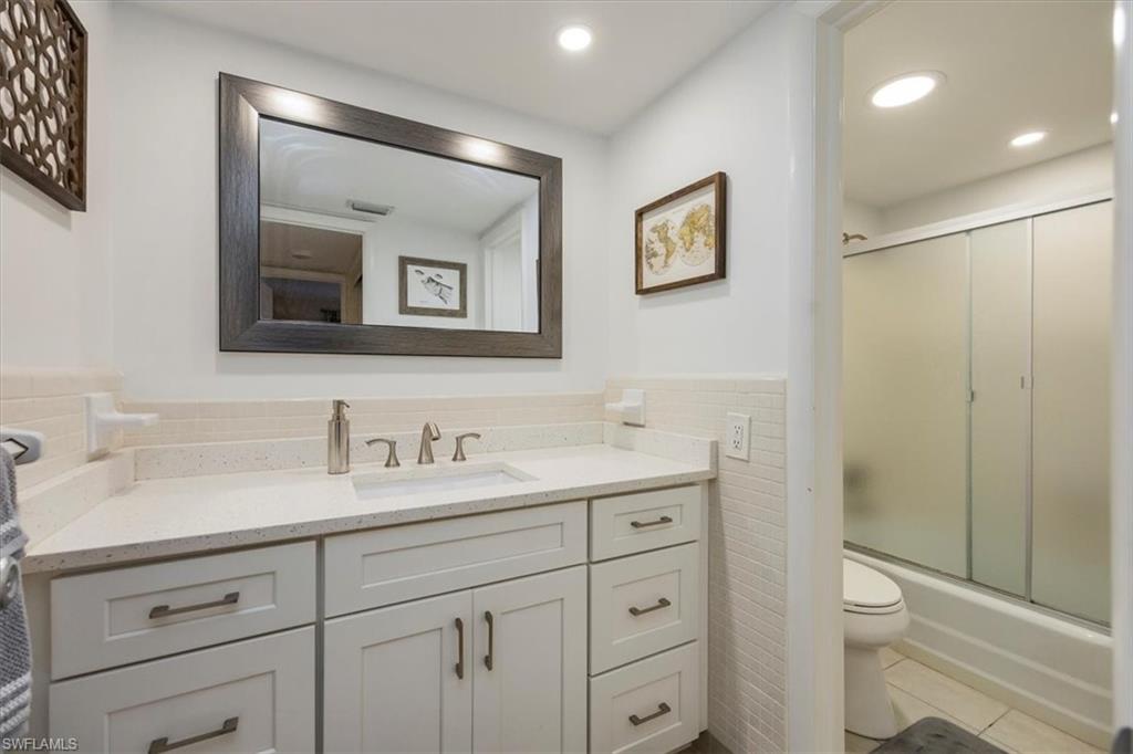 1900 Clifford Street, Unit 301 Fort Myers, FL 33901 - Photo 10 of 35 Bathroom with tile walls, vanity, tile patterned flooring, a wainscoted wall, and bath / shower combo with glass door