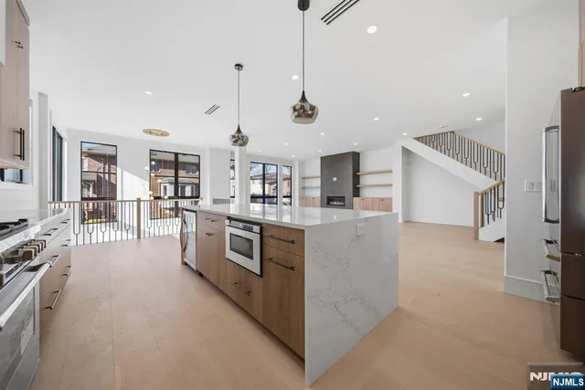 a kitchen with stainless steel appliances kitchen island a stove a sink a refrigerator and white cabinets with wooden floor