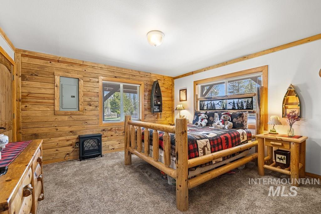 30 Redtail Lane McCall, ID 83638 - Photo 32 of 50 Bedroom featuring wood walls, dark carpet, a wood stove, and electric panel