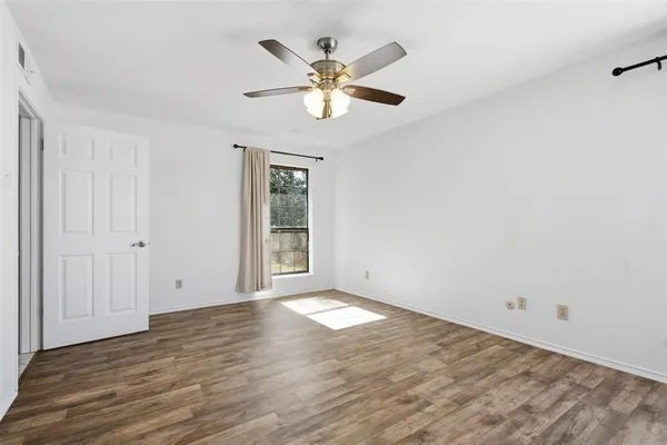 an empty room with wooden floor fan and windows