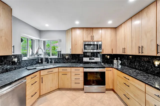 a large kitchen with granite countertop white cabinets sink and stainless steel appliances