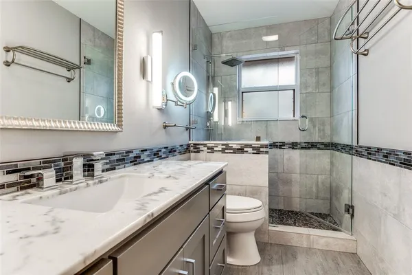 a bathroom with a granite countertop sink a toilet a mirror and shower