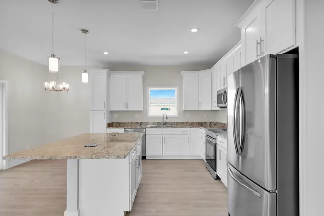 a kitchen with stainless steel appliances granite countertop a refrigerator a stove a sink and white cabinets