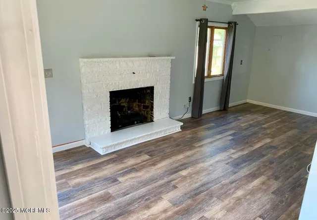 an empty room with wooden floor fireplace and windows