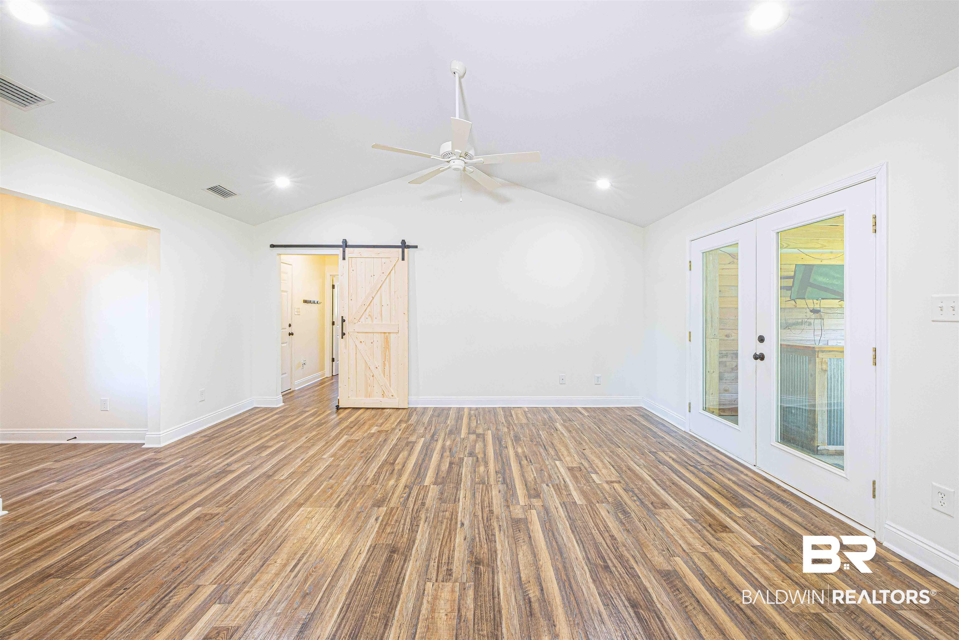 18675 Explorer Drive Loxley, AL 36551 - Photo 9 of 42 Empty room featuring a barn door, wood finished floors, french doors, lofted ceiling, and baseboards