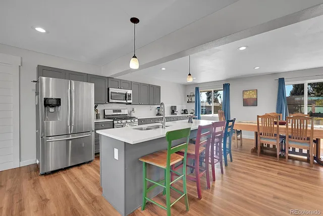 a kitchen with stainless steel appliances granite countertop a refrigerator a stove a sink dishwasher a dining table and chairs with wooden floor