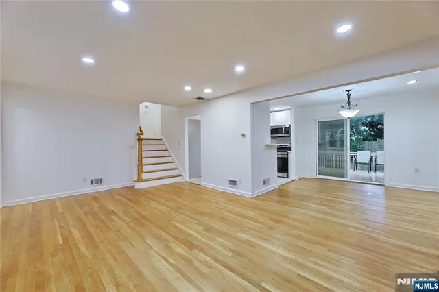 a view of an empty room with wooden floor and a kitchen