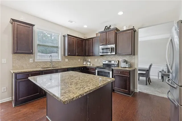a kitchen with kitchen island granite countertop a stove top oven a sink dishwasher a dining table and chairs