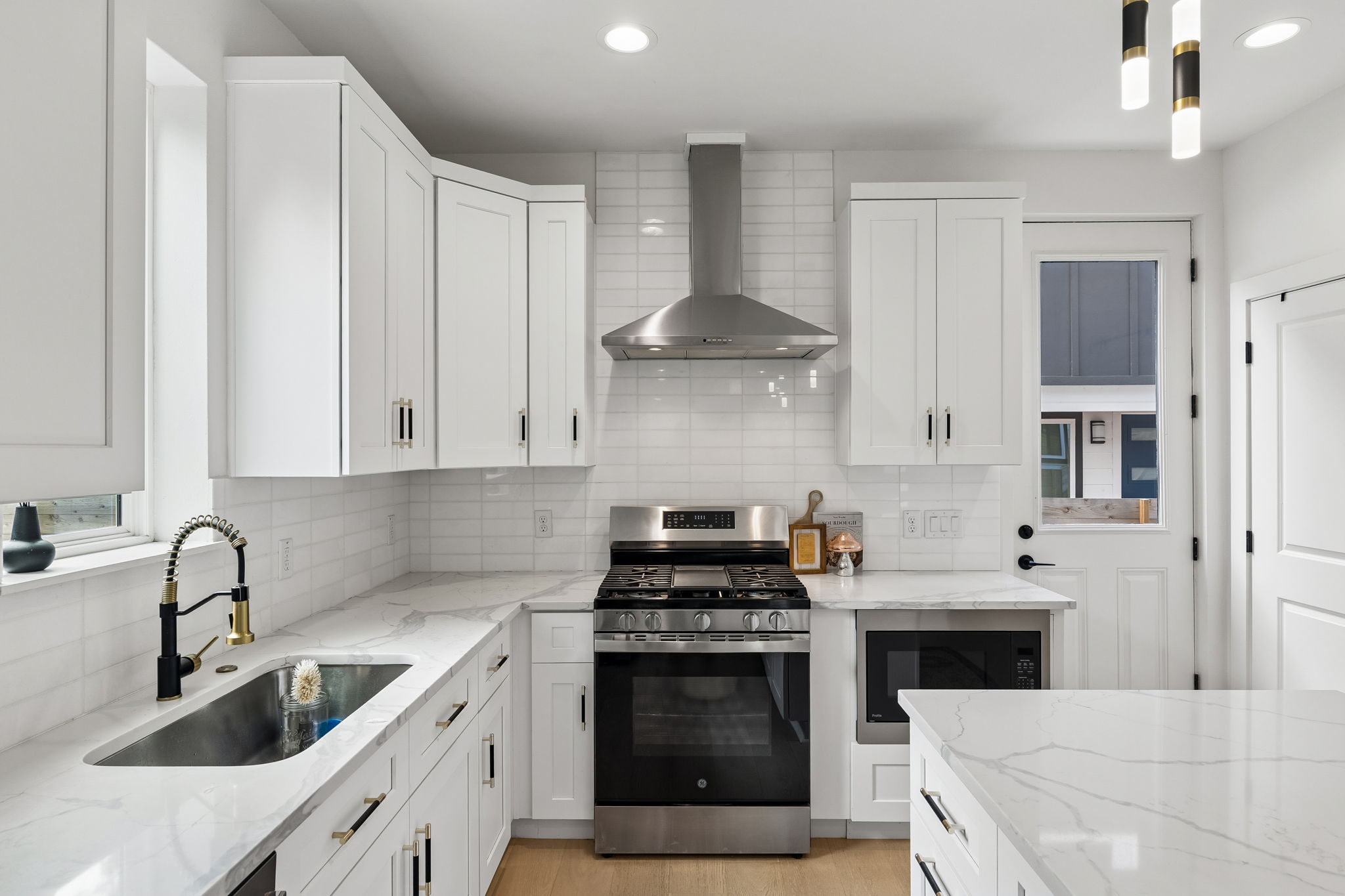 5305 Ledesma Road, Unit 1 Austin, TX 78721 - Photo 5 of 26 A close-up of the gourmet kitchen’s cooking wall. It features white shaker-style cabinetry with matte black hardware, a classic white subway tile backsplash, and high-end stainless steel GE appliances, including a gas range and a built-in microwave.