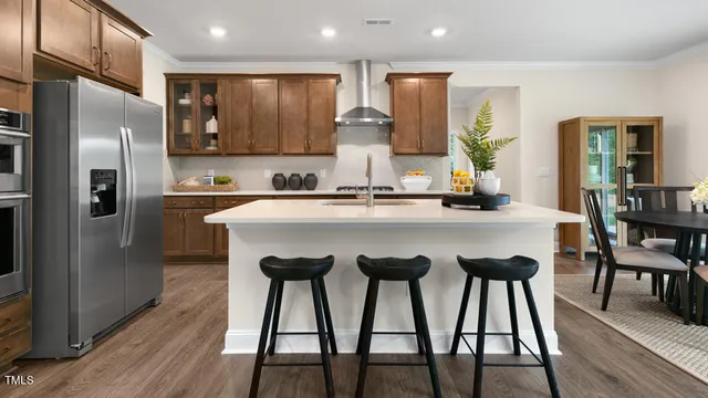 a kitchen with stainless steel appliances granite countertop a dining table chairs refrigerator and sink