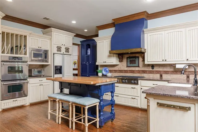 a kitchen with stainless steel appliances granite countertop a stove top oven a sink dishwasher and white cabinets with wooden floor