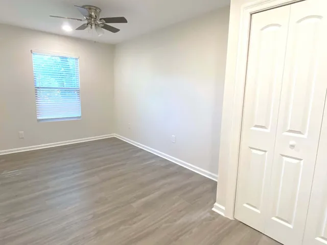 an empty room with wooden floor fan and windows