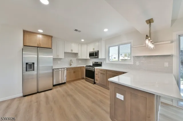 a large kitchen with stainless steel appliances kitchen island a sink dishwasher a refrigerator and white cabinets with wooden floor