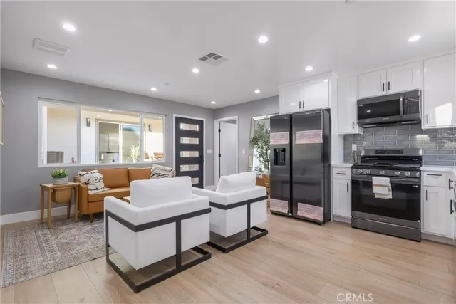 a living room with stainless steel appliances furniture windows and a kitchen view