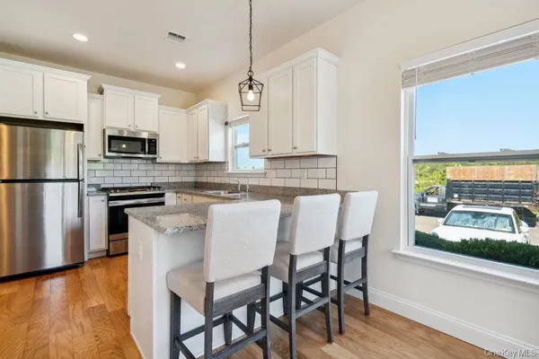 a kitchen with stainless steel appliances a microwave a stove a refrigerator and a dining table with wooden floor