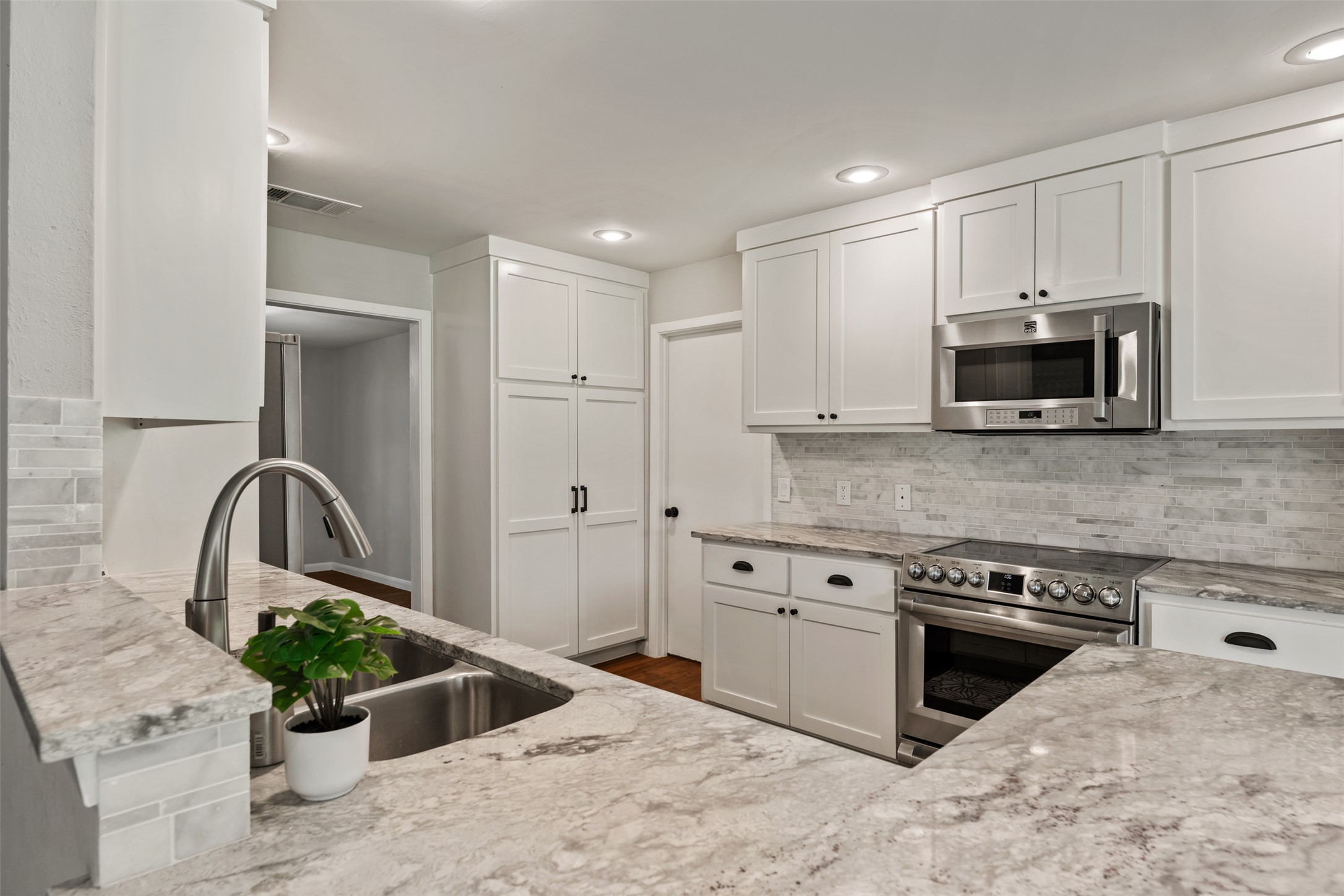 1600 Pin Oak Lane Round Rock, TX 78681 - Photo 18 of 40 Kitchen featuring stone countertops, white shaker-style cabinetry, stainless steel appliances, a stainless steel double basin sink with a gooseneck faucet, and a subway tile backsplash