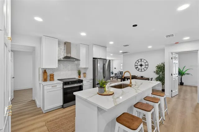 a living room with stainless steel appliances furniture wooden floor and a kitchen view