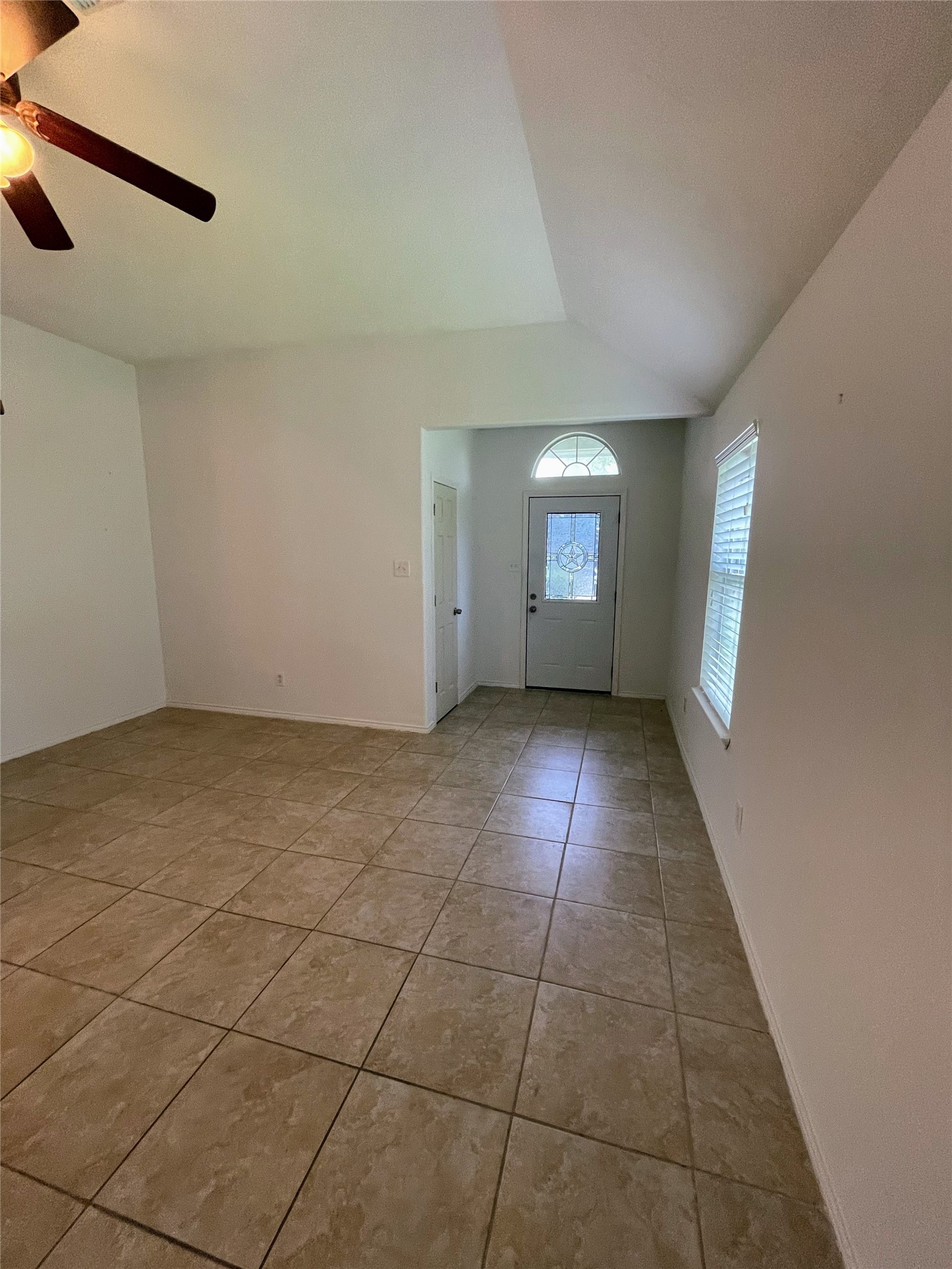 4010 Bealey Lane Houston, TX 77047 - Photo 6 of 29 The living room features a tiled floor, neutral walls, a ceiling fan, and natural light from a window and a decorative front door. The space has a high ceiling and a cozy entryway.