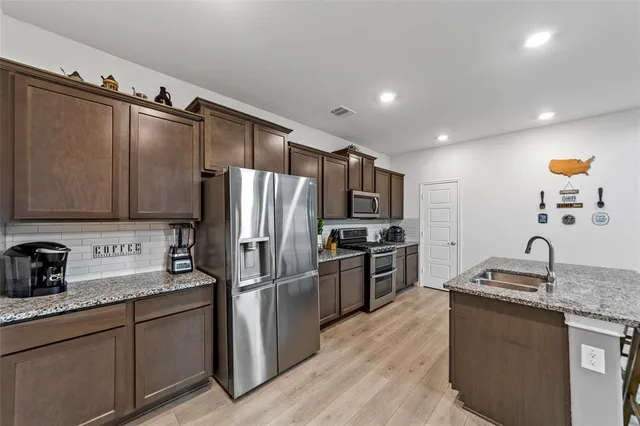 a kitchen with granite countertop stainless steel appliances a refrigerator stove top oven and sink