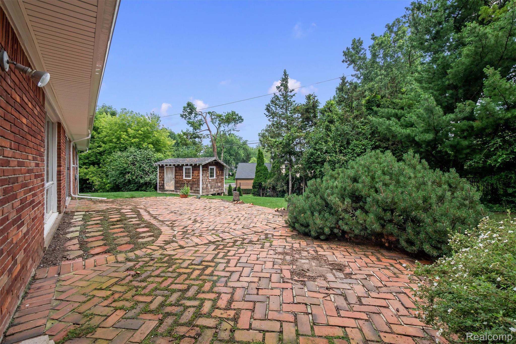1151 Peveril Road Bloomfield Hills, MI 48304 - Photo 37 of 39 Expansive brick patio featuring a herringbone pattern, bordered by mature evergreens and landscaping